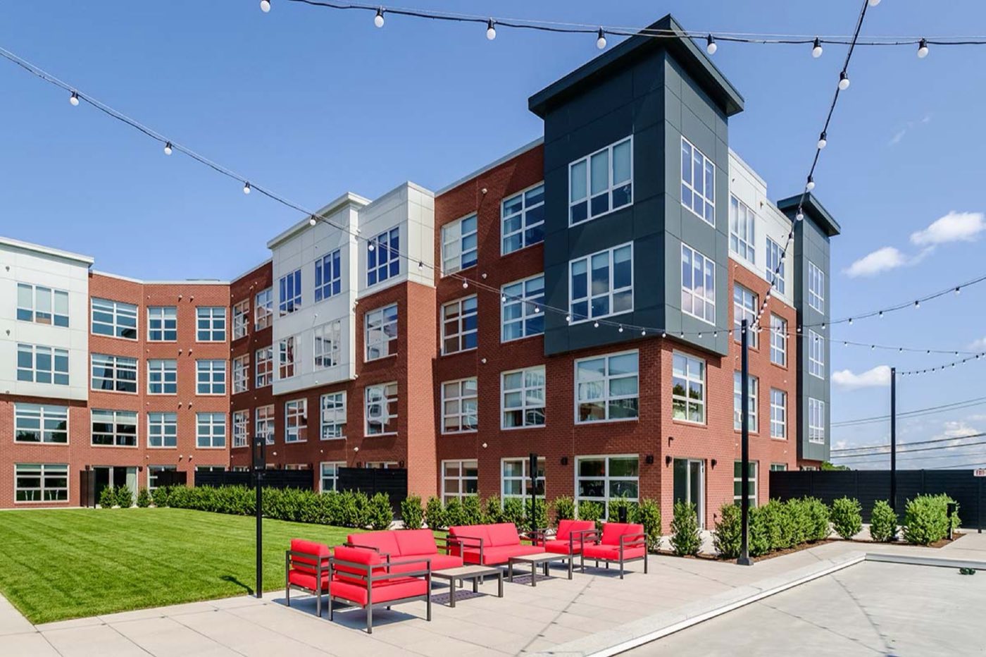 The brick and panel exterior of Trademark Fairfield with string lights over the lawn